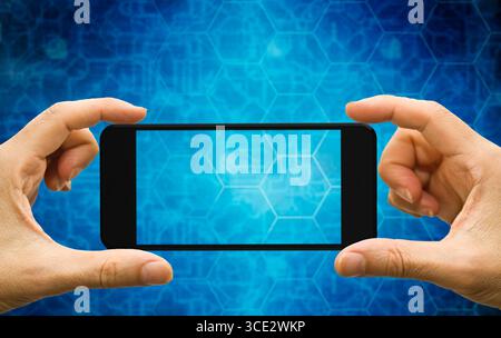 hands holding a blank smartphone against digital blue hexagon background, futuristic technology concept Stock Photo