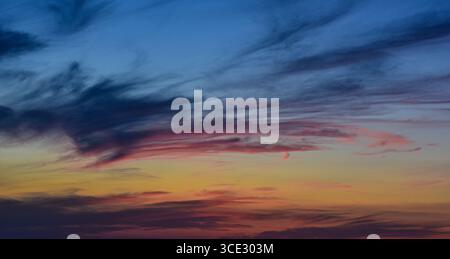 Fiery colors of sunset painting the sky with delicate cloudy textures. Stock Photo