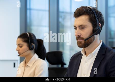 Two customer support agents in a modern office, wearing headsets and working attentively on support tasks. Stock Photo