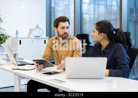Two colleagues are collaborating and sharing ideas in a vibrant workspace. Incorporating modern technology and laptops, they focus on effective communication and teamwork Stock Photo