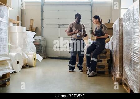 Long shot of two diverse warehouse workers having lunch time, copy space Stock Photo
