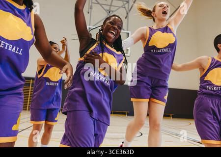 A group of energetic young adults in team uniforms celebrates a successful game, showcasing teamwork and enthusiasm on an indoor basketball court. Stock Photo