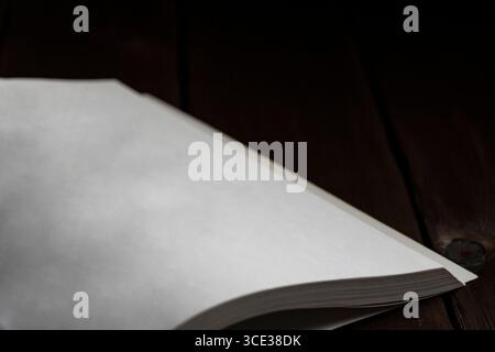 Minimalist close-up of a blank open book on a dark wooden surface. Ideal for mockups, writing or reading concepts, and creative backgrounds Stock Photo