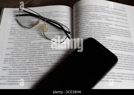 Close-up of eyeglasses and smartphone on an open book. Symbol of focus, distraction, digital life, or learning. Ideal for education, reading, and tech Stock Photo