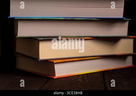 Close-up of a stack of colorful hardcover books lying on a dark wooden surface. Perfect for themes related to education, literature, learning, and stu Stock Photo