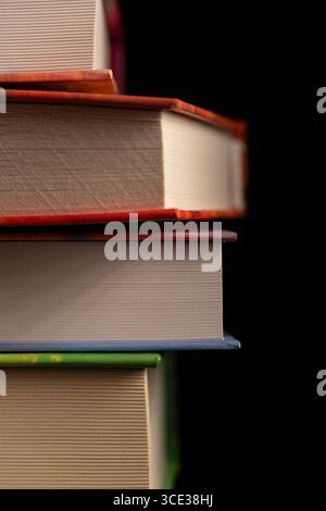 Close-up of a vertical stack of hardcover books with colorful bindings and textured pages, isolated on a black background. Ideal for education, librar Stock Photo