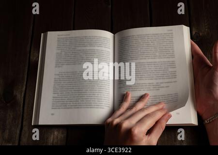 A close-up image of hands flipping through the pages of an open book on a dark wooden surface, emphasizing the tactile experience of reading Stock Photo