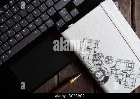 A close-up of an architect s workspace with a laptop keyboard, architectural sketches in a notebook, and a pen on a wooden desk, evoking themes of des Stock Photo