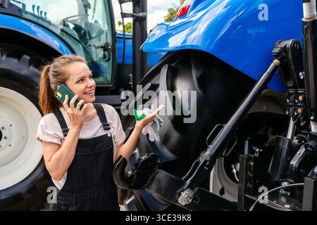 Woman farmer standing near tractor and talking on cellphone outdoors Stock Photo
