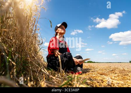 Female modern farmer with digital tablet resting by cereal field in summer Stock Photo