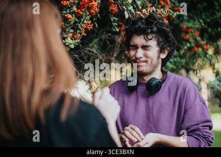 Young man squinting with headphones in a green and vibrant outdoors Stock Photo