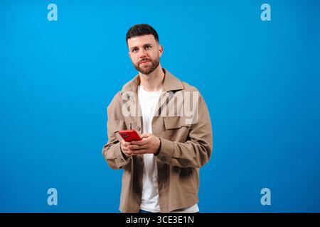 Man smiling while using a red smartphone against a bright blue background Stock Photo