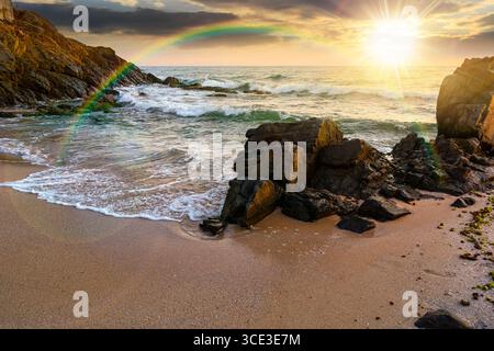 landscape by the sea at sunset in summer. beautiful beach with rocks washed by calm waves in evening light. view to horizon under rainbow and  blue sk Stock Photo
