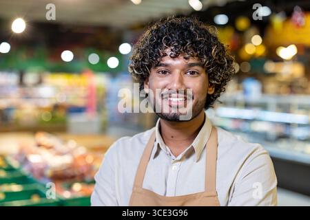 A cheerful grocery store worker confidently posing in an aisle, surrounded by colorful items, symbolizing positive service and teamwork. Stock Photo