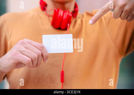 Smiling young man pointing at camera and holding blank business card outdoors Stock Photo