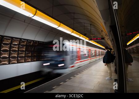 A Prague metro train arrives at Narodni trida station, with passengers waiting on the tiled platform as its motion blurs past. Stock Photo