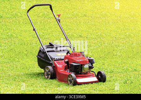 Red lawn mower isolated on green grass background. Stock Photo