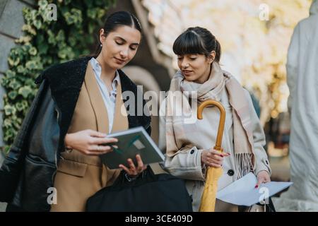 Two businesswomen reviewing documents outdoors during a professional meeting Stock Photo