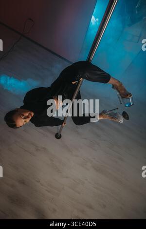 Woman performing artistic pole dance in a dynamic studio setting Stock Photo