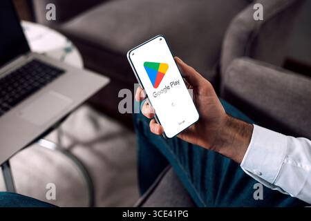 Google play on mobile phone screen. Man user holding a smartphone showing play store application launch screen. Stock Photo