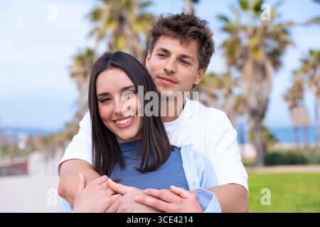 Happy young couple hugging and smiling on palm-lined seaside promenade Stock Photo