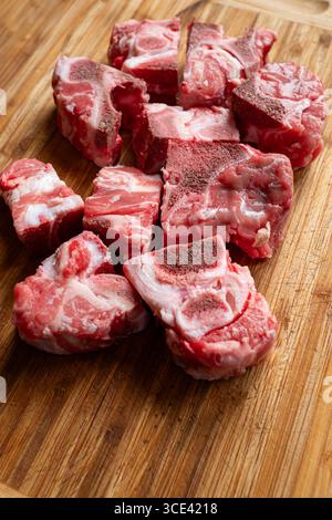 Raw, cut, fresh beef ox tail pieces used for soup broth or stews. Top down view, set on wooden kitchen board, close up shot, no people Stock Photo