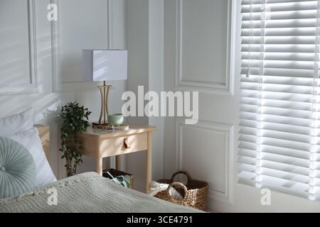 Bedside table with lamp and other decor near bed indoors Stock Photo
