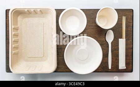An eco friendly disposable tableware set includes tray, bowls, cup, spoon, and chopsticks on wooden surface, promoting sustainability Stock Photo