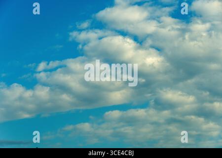 Bright white clouds float gently in a clear blue sky, creating a picturesque view during a sunny afternoon in early autumn. Stock Photo