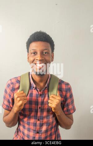 Smiling African male student in casual plaid shirt with backpack, posing against a plain background. Concept: back to school, youth education, student Stock Photo