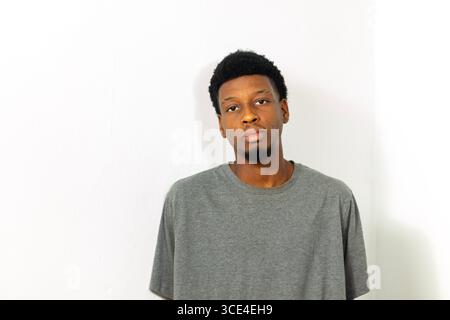 young teenager man in plain grey t-shirt, posing against white background. Concept: reflection, decision making, planning, mental focus, progress Stock Photo