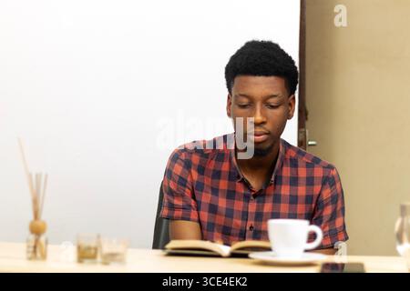 African young man studying at table with coffee and notebook. Concept: modern student lifestyle, productivity, learning in cafe, academic preparation. Stock Photo
