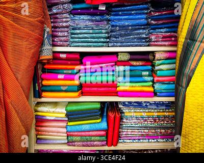 Stacks of vibrant and colorful fabric rolls on shelves in a textile shop, showcasing a variety of patterns and materials malaysia Stock Photo