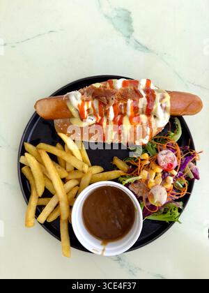 Top view of a delicious hot dog with sauces, fries, and fresh salad on a black plate with dipping sauce malaysia Stock Photo