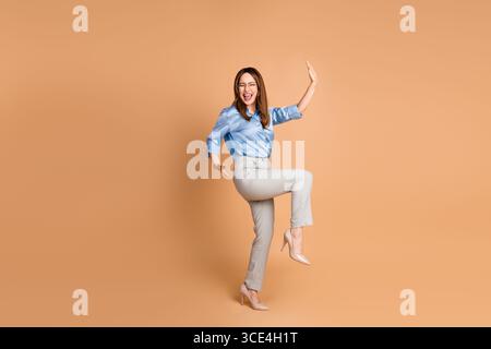 Cheerful businesswoman in blue blouse posing joyfully against beige background symbolizing success and positivity Stock Photo