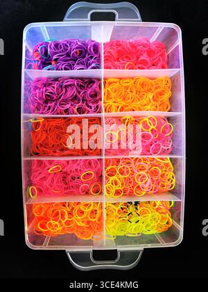 Numerous rubber bands are neatly arranged in a clear storage container, displaying vibrant colors like purple, pink, and orange. Stock Photo