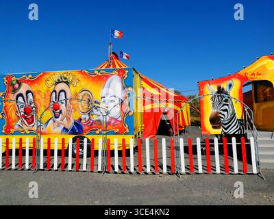 Vibrant circus tent adorned with bright colors and clown imagery, alongside distinctive vehicles. France Stock Photo