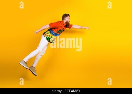 Young bearded man in vibrant tropical shirt posing energetically against bright yellow background embodying summer vibes Stock Photo
