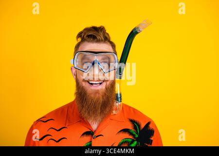 Cheerful bearded man wearing snorkeling gear and tropical shirt poses cheerfully against a vibrant yellow background Stock Photo