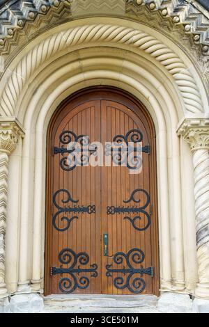 Ornate wooden arched door with decorative wrought iron hinges at University College. Stock Photo