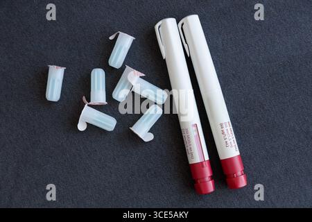 top shot features two injection pens alongside several protective caps scattered on a dark surface, highlighting essential medical supplies used in he Stock Photo