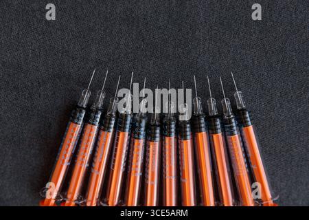 This image showcases a series of syringes with orange barrels and clear tips, meticulously arranged in a row on a dark surface, commonly used in medic Stock Photo