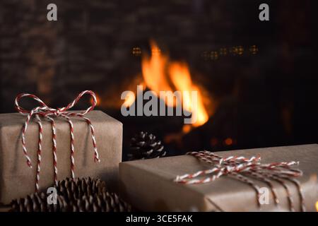 Closeup Christmas gifts wrapped in simple brown paper tied with red and white string in front of a fireplace at home Stock Photo