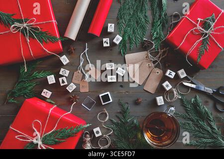 Top down view of Christmas gift boxes wrapped in red paper with tags and decorations on wooden table Stock Photo