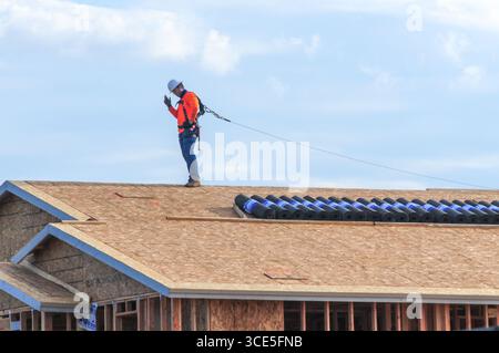 Mesa, Arizona, USA. 15th Aug, 2025. A construction worker secured with a safety harness signals while working on the roof of a home under construction in a residential development in the Phoenix metro area. Residential, commercial, and data center construction continues across the region as Maricopa County's real estate market cools after years of rapid gains, with more listings easing pressure on buyers. (Credit Image: © Eduardo Barraza/ZUMA Press Wire) EDITORIAL USAGE ONLY! Not for Commercial USAGE! Stock Photo