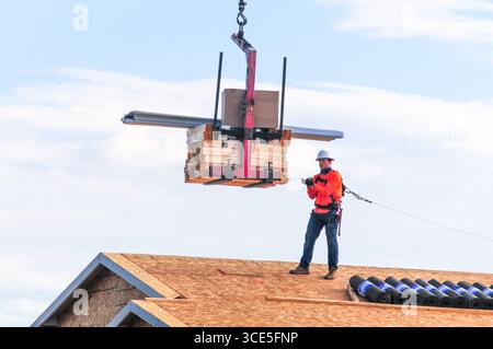 Mesa, Arizona, USA. 15th Aug, 2025. A construction worker guides a crane-delivered load of lumber onto the roof of a new home under construction in a residential development in the Phoenix metro area. Residential, commercial, and data center construction continues across the region as Maricopa County's real estate market cools after years of rapid gains, with more listings easing pressure on buyers. (Credit Image: © Eduardo Barraza/ZUMA Press Wire) EDITORIAL USAGE ONLY! Not for Commercial USAGE! Stock Photo