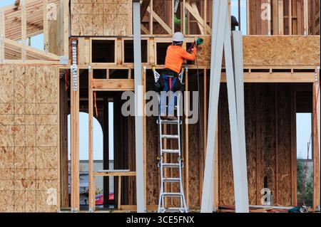 Mesa, Arizona, USA. 15th Aug, 2025. A construction worker stands on a ladder while installing siding on a home under construction in a residential development in the Phoenix metro area. Residential, commercial, and data center construction continues across the region as Maricopa County's real estate market cools after years of rapid gains, with more listings easing pressure on buyers. (Credit Image: © Eduardo Barraza/ZUMA Press Wire) EDITORIAL USAGE ONLY! Not for Commercial USAGE! Stock Photo