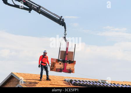 Mesa, Arizona, USA. 15th Aug, 2025. A construction worker guides a crane-delivered load of lumber onto the roof of a new home under construction in a residential development in the Phoenix metro area. Residential, commercial, and data center construction continues across the region as Maricopa County's real estate market cools after years of rapid gains, with more listings easing pressure on buyers. (Credit Image: © Eduardo Barraza/ZUMA Press Wire) EDITORIAL USAGE ONLY! Not for Commercial USAGE! Stock Photo