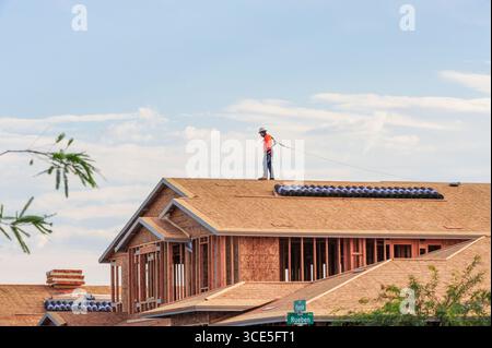 Mesa, Arizona, USA. 15th Aug, 2025. A construction worker secured with a safety harness walks along the roof of a home under construction in a residential development in the Phoenix metro area. Residential, commercial, and data center construction continues across the region as Maricopa County's real estate market cools after years of rapid gains, with more listings easing pressure on buyers. (Credit Image: © Eduardo Barraza/ZUMA Press Wire) EDITORIAL USAGE ONLY! Not for Commercial USAGE! Stock Photo