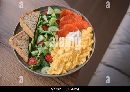 Overhead view of a plate of scrambled eggs, smoked salmon, mixed salad, multigrain bread and cream cheese on a table Stock Photo